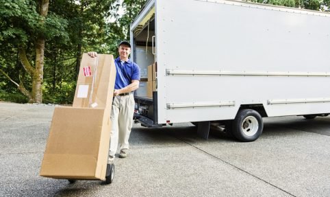 Photo of a delivery man with cardboard boxes on hand truck.